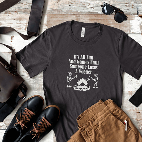 Our Camping tee features two adorable stick figure people roasting wieners over a cozy campfire. And with the hilarious slogan "It's All Fun & Games Until Someone Loses A Wiener," you'll be the life of the party at any camping trip!